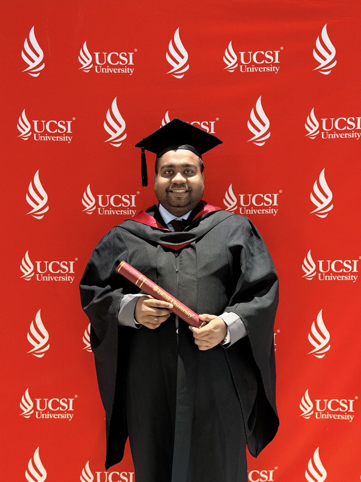 Holding the degree scroll in front of the UCSI backdrop